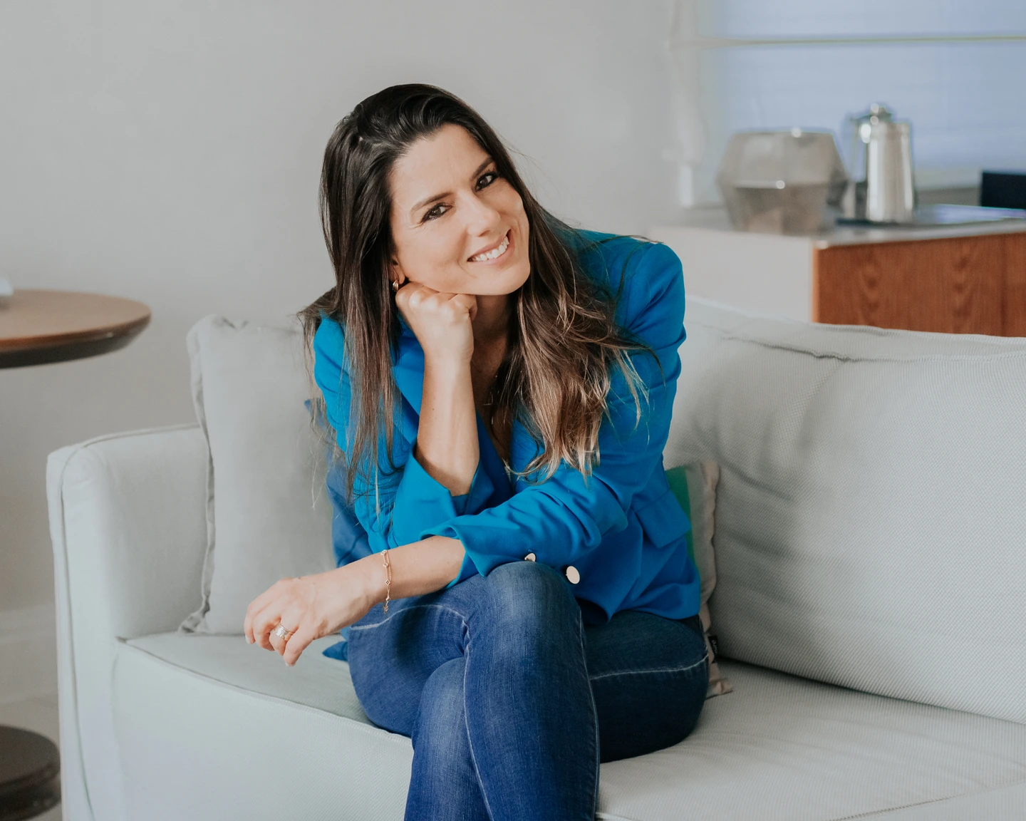 Renata André sorrindo, sentada em um sofá.